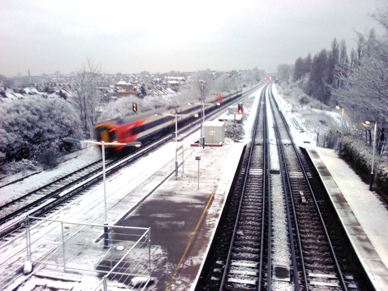 A fast train rushes through a snowy Earlsfield station